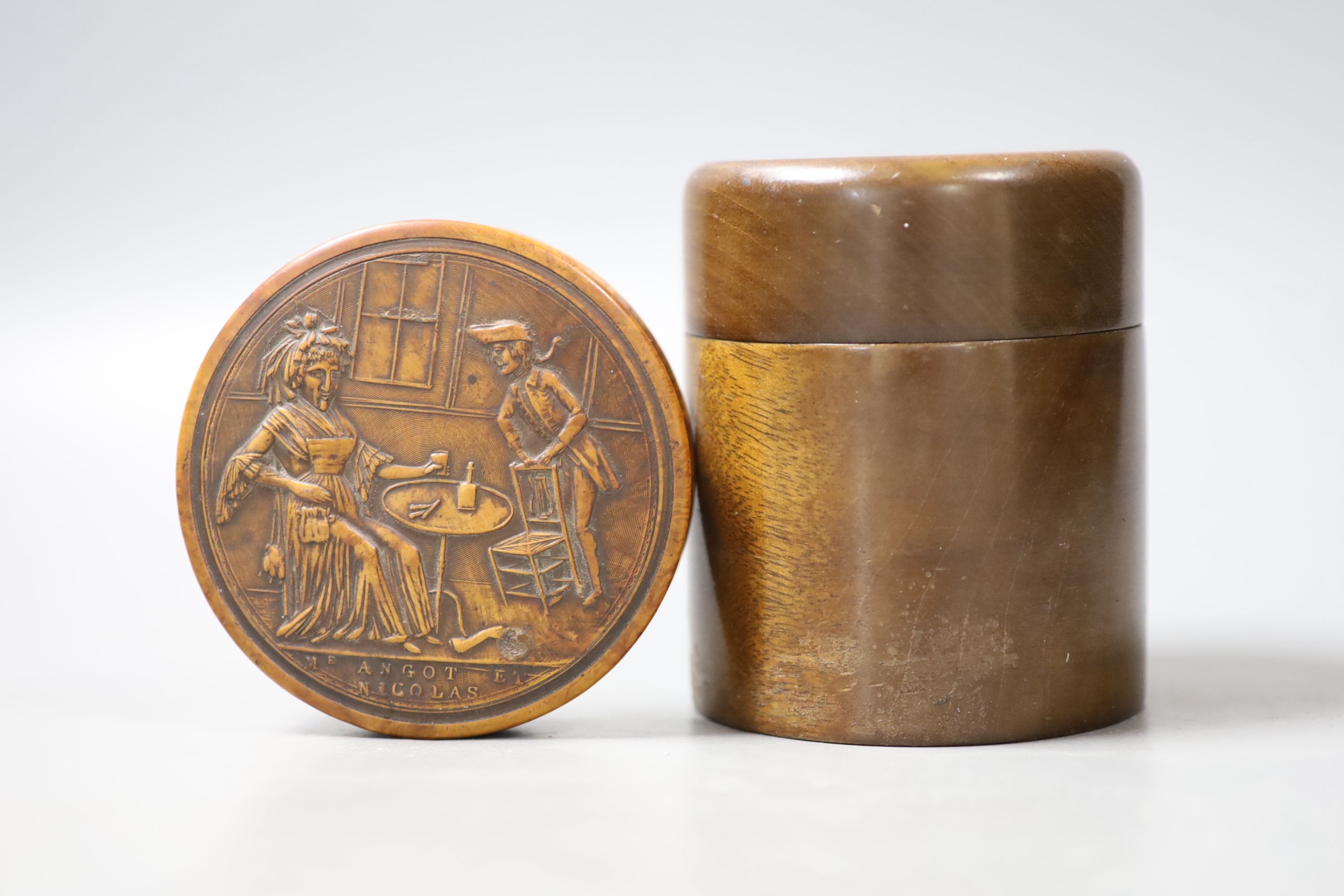 A French press moulded burr wood snuff box of circular form, decorated in semi-relief to the top with a scene entitled 'Nicolas Angot', 8.2cm and a wood case